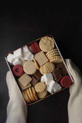 Female hands holding a metal box of assorted cookies