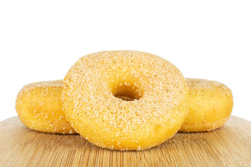 Group of three whole sweet golden mini cinnamon donut on bamboo cutting board isolated on white background