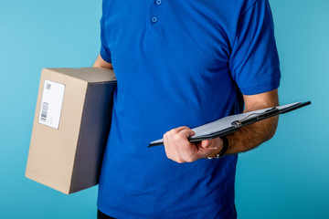 Cropped view of delivery man holding clipboard and cardboard package isolated on blue