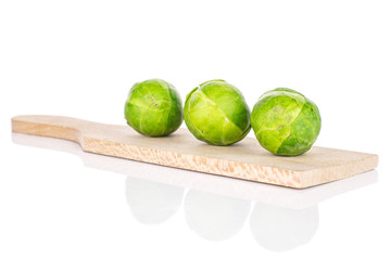 Group of three whole fresh green brussels sprout on small wooden cutting board isolated on white background