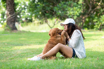 Asian woman playing and hug young dog golden retriever friendship dog in outdoor the nature park background. Lifestyle Concept.