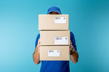 Delivery man holding cardboard packages with qr codes and barcodes isolated on blue