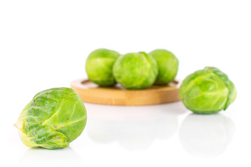 Group of five whole fresh green brussels sprout on bamboo coaster isolated on white background
