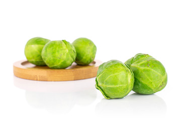 Group of five whole fresh green brussels sprout on bamboo coaster isolated on white background