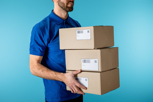 Cropped view of delivery man holding cardboard packages isolated on blue