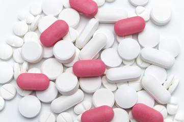 Prescription drugs, pills and tablets of different colors between white and pink colors . On white background. Selective focus.