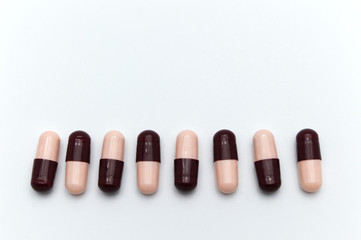 Prescription drugs, capsules of soft pink and dark reddish brown colors all mixed in. On white background.