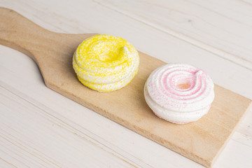 Group of two whole pink and yellow sweet meringue on small wooden cutting board on white wood