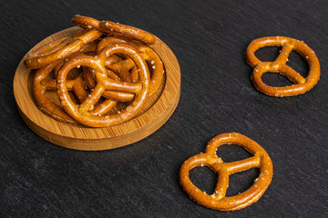 Lot of whole salty brown pretzel on bamboo coaster on grey stone