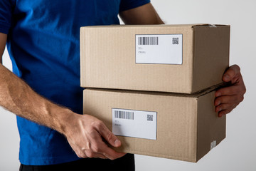 Cropped view of courier holding boxes with barcodes and qr codes on cards isolated on grey