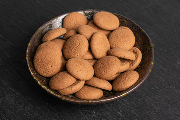Lot of whole sweet brown chocolate sponge biscuit in dark ceramic bowl on grey stone