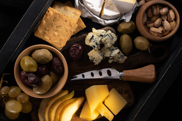 Top view of food composition of cheese, dried olives, fruits, pistachios and crackers on wooden tray