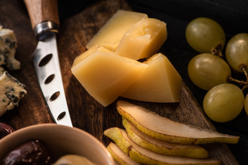 Selective focus of grana padano with pieces of pear, bowl of olives, knife, dorblu, grapes on...