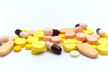 Prescription drugs, pills, capsules and vitamin C tablets of different colors all mixed in. On white background. Selective focus.