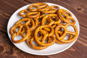 Lot of whole salty brown pretzel on white ceramic plate on brown wood