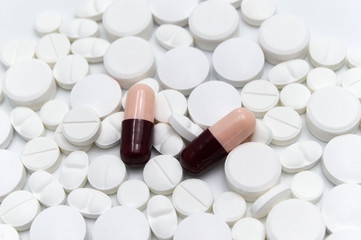 Prescription drugs, pills and tablets of different colors between red and dark gray colors all mixed in a capsules and white tablets . On a white background. Selective focus.