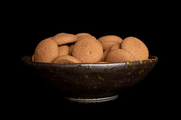 Lot of whole sweet brown chocolate sponge biscuit in dark ceramic bowl isolated on black glass