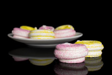 Group of eight whole pink and yellow sweet meringue on white ceramic plate isolated on black glass