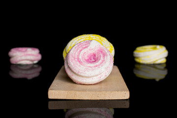 Group of four whole pink and yellow sweet meringue on small wooden cutting board isolated on black glass