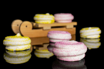 Group of six whole pink and yellow sweet meringue with wooden sledge isolated on black glass