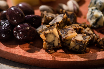 Selective focus of pieces of nut cheese with olives on round wooden board