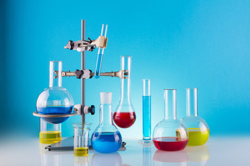 Biological laboratory. A tripod with variety of chemical glass and colored liquids on a blue background