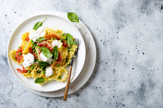 Italian pasta mafalde with green peas, prosciutto, burrata,  and spinach