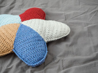 Closeup hand made multicolored yarn knitted pillow in the shape of a starfish on a gray background. Natural materials for the interior. Chemical free textile