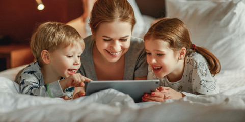 happy family mother and children with tablet computer at home in bed in   evening.