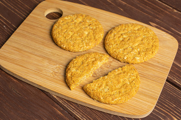 Group of two whole two halves of sweet golden oat cookie on bamboo cutting board on brown wood