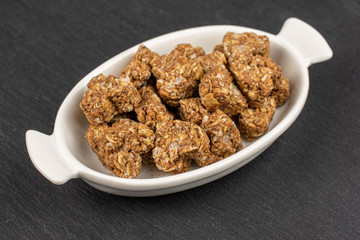 Lot of whole healthy brown cereal heart with cocoa in white oval ceramic bowl on grey stone