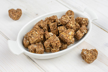 Lot of whole healthy brown cereal heart with cocoa in white oval ceramic bowl on white wood
