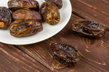 Lot of whole dry brown date fruit on white ceramic plate on brown wood