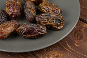 Lot of whole dry brown date fruit on gray ceramic plate on brown wood
