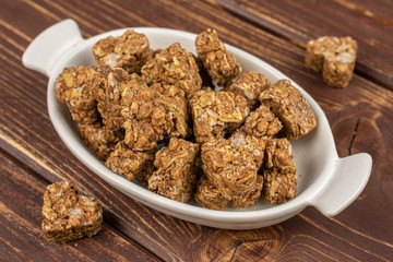 Lot of whole healthy brown cereal heart with cocoa in white oval ceramic bowl on brown wood