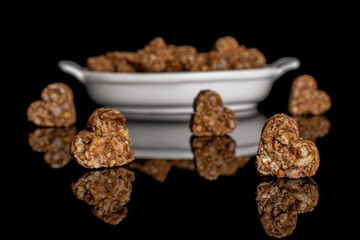 Lot of whole healthy brown cereal heart with cocoa in white oval ceramic bowl isolated on black glass