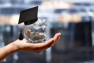 Graduation hat on a glass piggy bank with money in hand