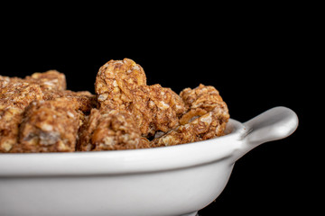 Lot of whole healthy brown cereal heart with cocoa closeup in white oval ceramic bowl isolated on black glass