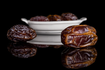 Group of five whole dry brown date fruit in white oval ceramic bowl isolated on black glass