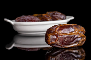 Group of four whole dry brown date fruit in white oval ceramic bowl isolated on black glass