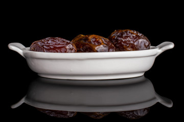 Group of three whole dry brown date fruit in white oval ceramic bowl isolated on black glass