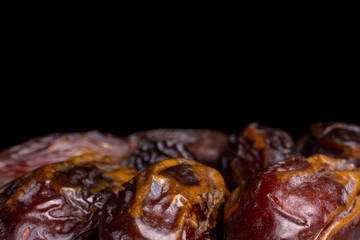 Lot of whole dry brown date fruit closeup isolated on black glass