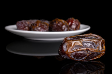 Group of five whole dry brown date fruit on white ceramic plate isolated on black glass