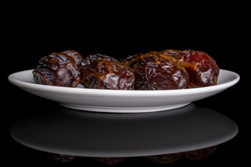 Group of four whole dry brown date fruit on white ceramic plate isolated on black glass