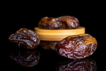Group of four whole dry brown date fruit on bamboo coaster isolated on black glass