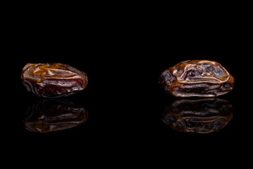 Group of two whole dry brown date fruit isolated on black glass