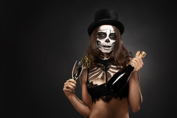Fototapeta na wymiar Halloween girl with skull makeup for Halloween on a black background holds champagne in her hands
