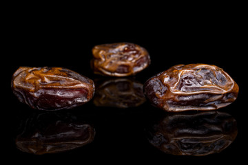 Group of three whole dry brown date fruit isolated on black glass