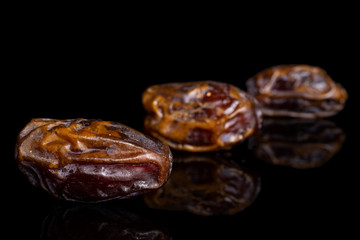 Group of three whole dry brown date fruit placed diagonally isolated on black glass