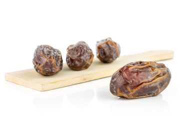 Group of four whole dry brown date fruit on small wooden cutting board isolated on white background